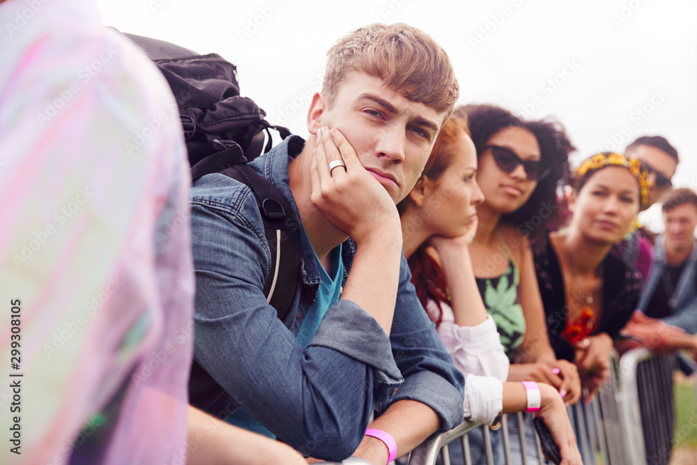 Obraz premium Group Of Young Friends Waiting Behind Barrier At Entrance To Music Festival Site