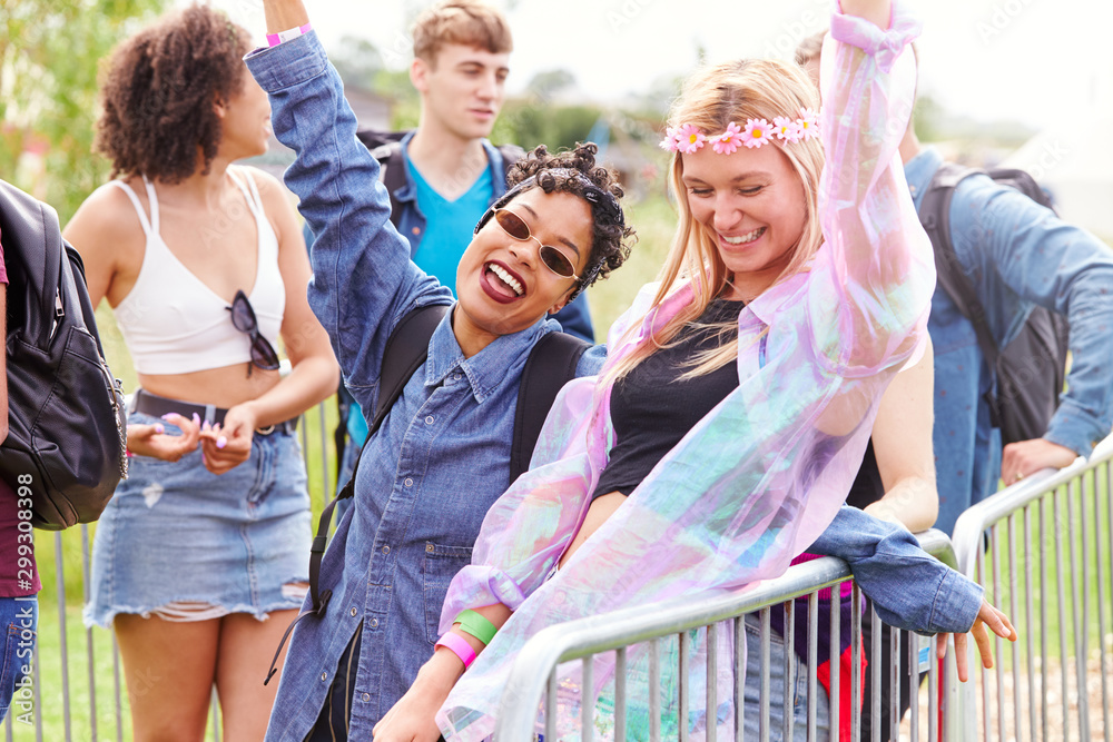 Fototapeta premium Portrait Of Female Friends Waiting Behind Barrier At Entrance To Music Festival Site