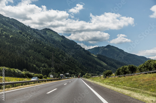 Autobahn or highway with a bridge in the mountains with clear marking surrounded by vibrant green trees under blue sky. Mountain in the background. The Alps, Austria