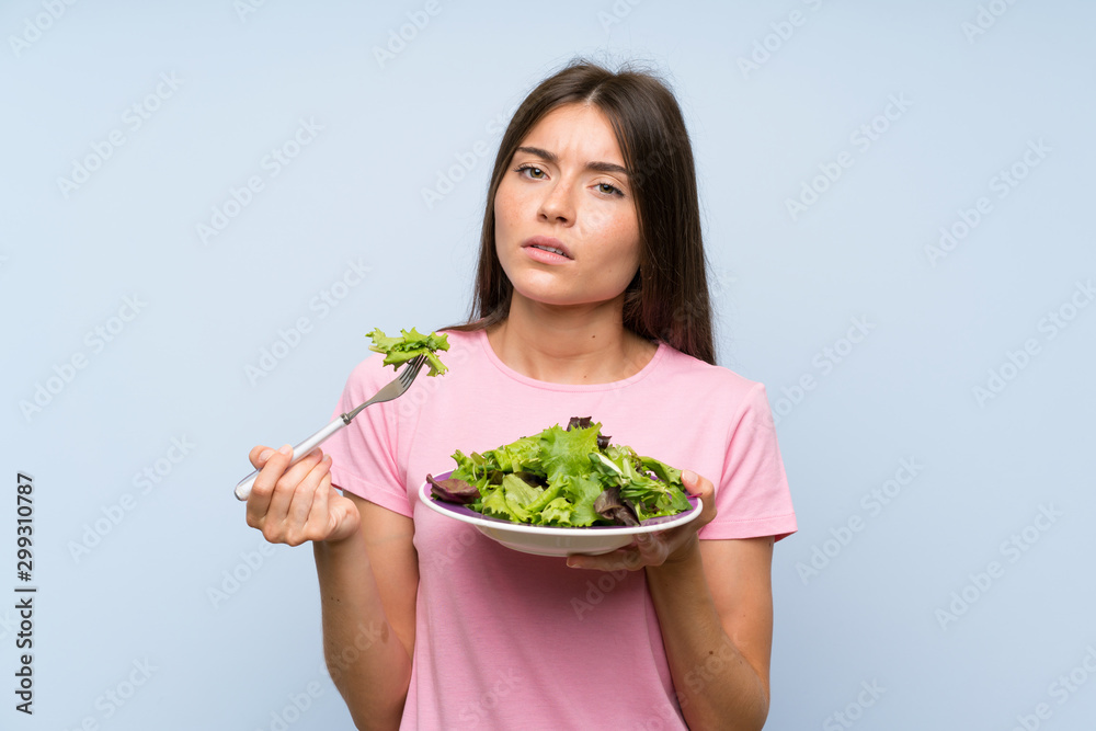 Young woman with salad over isolated blue background Young woman with salad over isolated blue background
