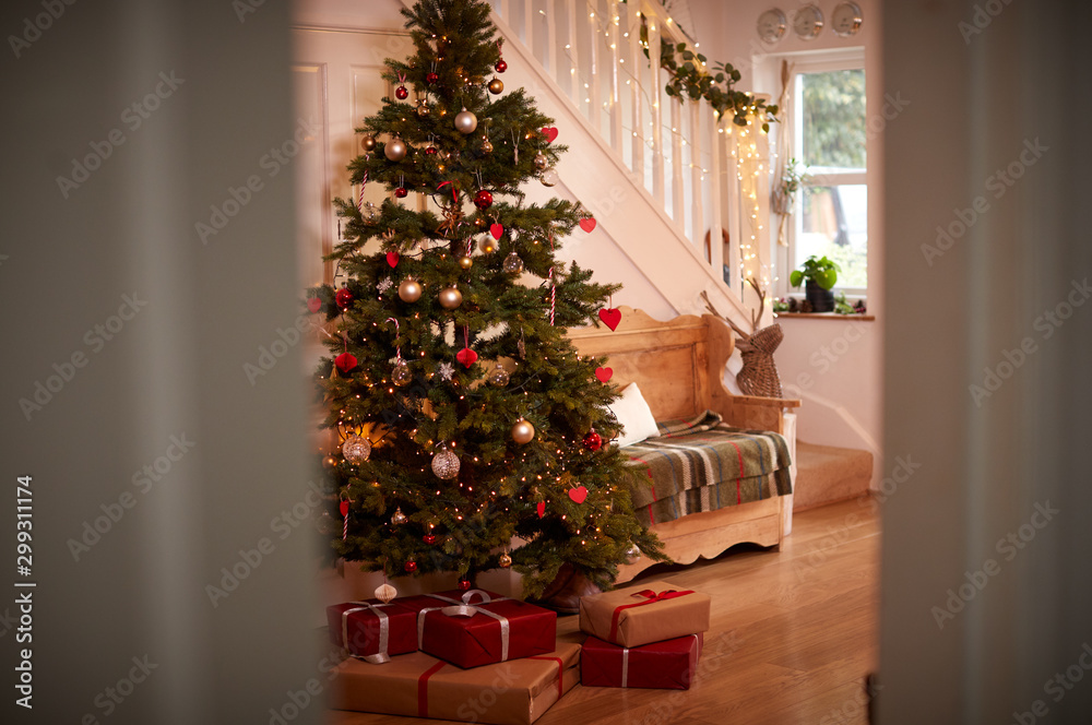 Hallway Of Home Decorated For Christmas With Tree And Presents Viewed Through Open Door