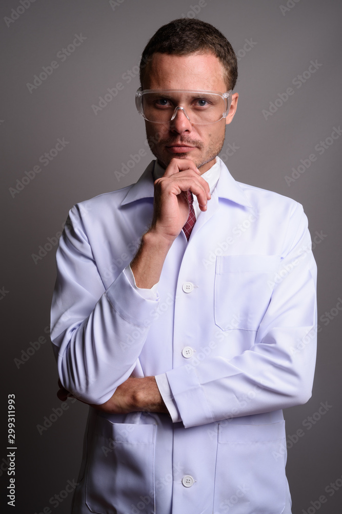Handsome man doctor wearing protective glasses against gray back Handsome man doctor wearing protective glasses against gray back