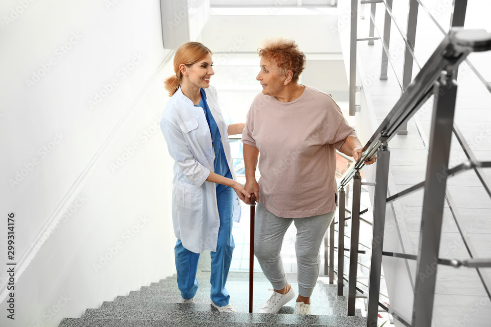 Nurse assisting elderly woman on stairs indoors