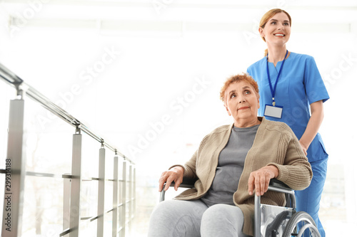 Nurse assisting elderly woman in wheelchair indoors. Space for text
