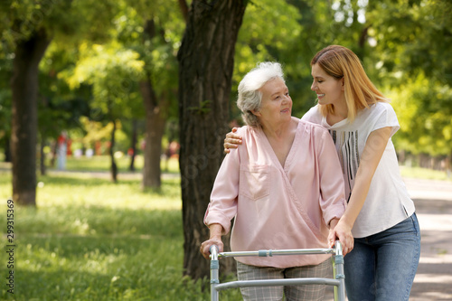 Caretaker helping elderly woman with walking frame outdoors photo