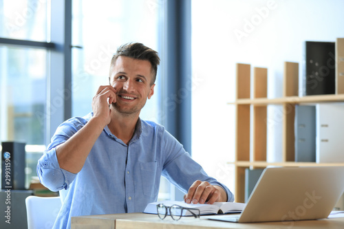 Foto Male business trainer talking on phone while working with laptop in office