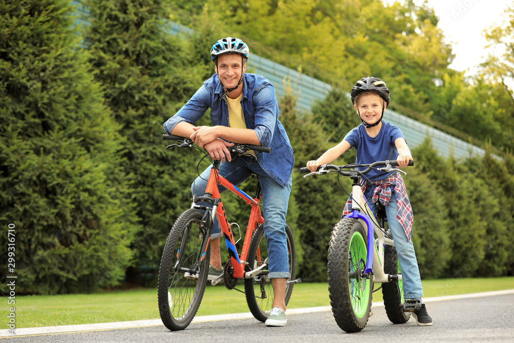 Dad and son riding modern bicycles outdoors Dad and son riding modern bicycles outdoors