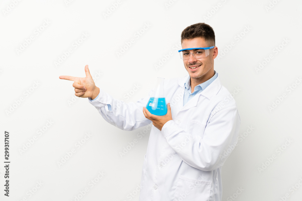 Young scientific holding laboratory flask over isolated background pointing finger to the side Young scientific holding laboratory flask over isolated background pointing finger to the side