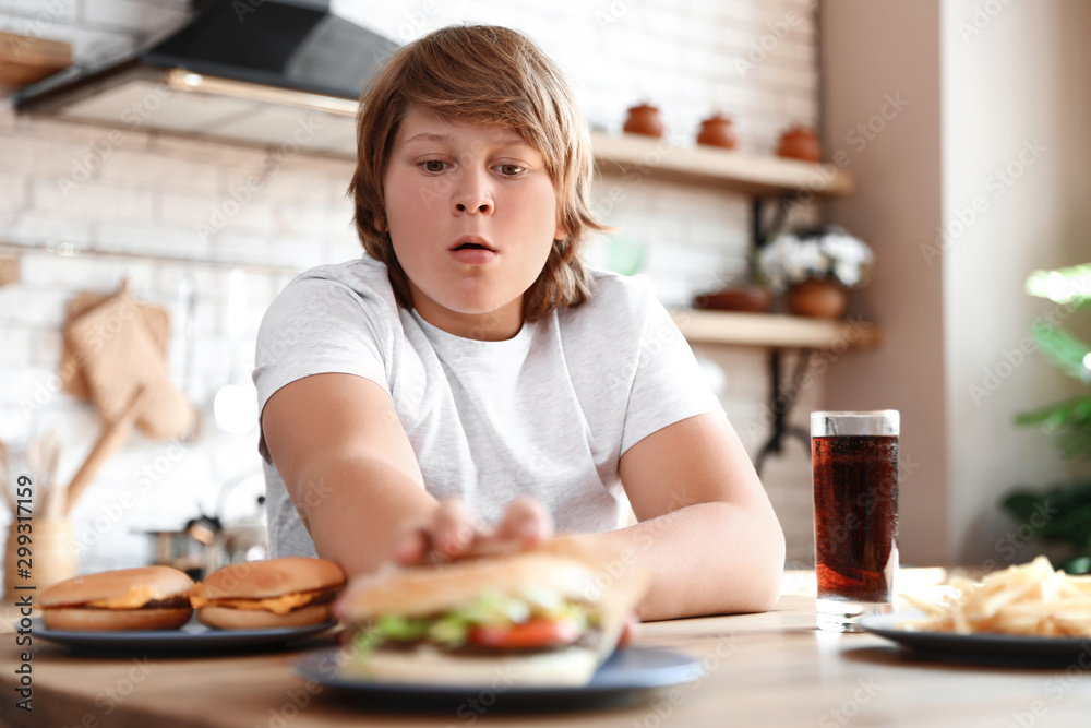 Emotional overweight boy at table with fast food in kitchen Emotional overweight boy at table with fast food in kitchen