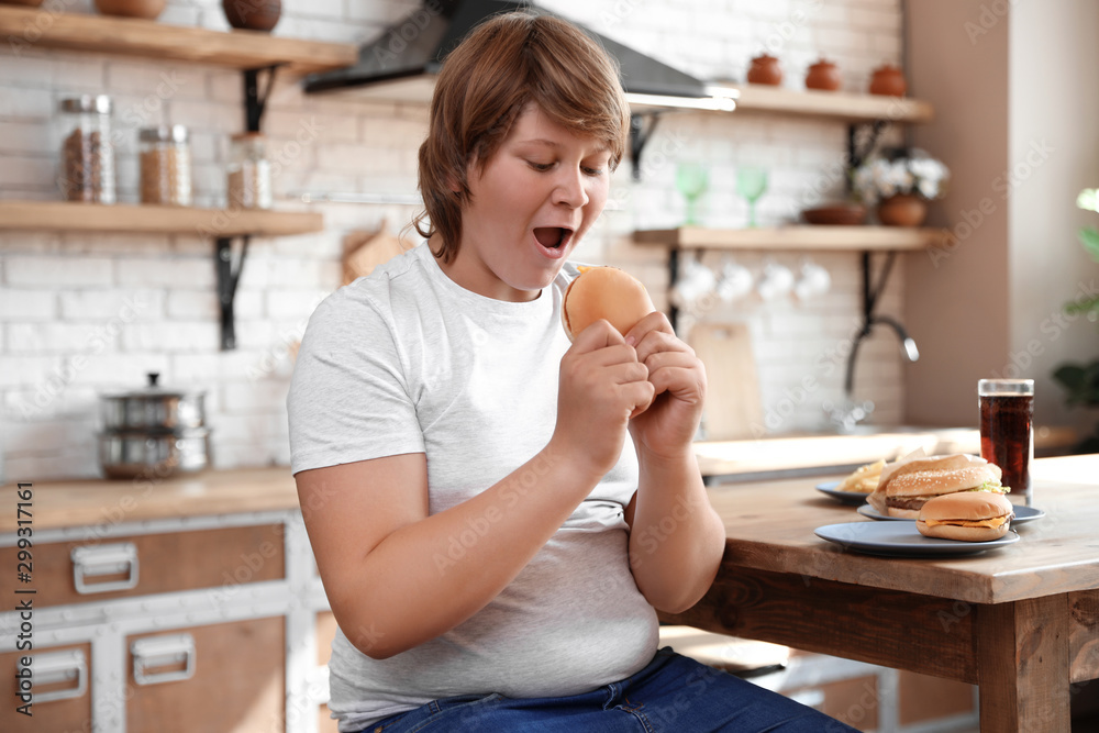Emotional overweight boy at table with fast food in kitchen Emotional overweight boy at table with fast food in kitchen