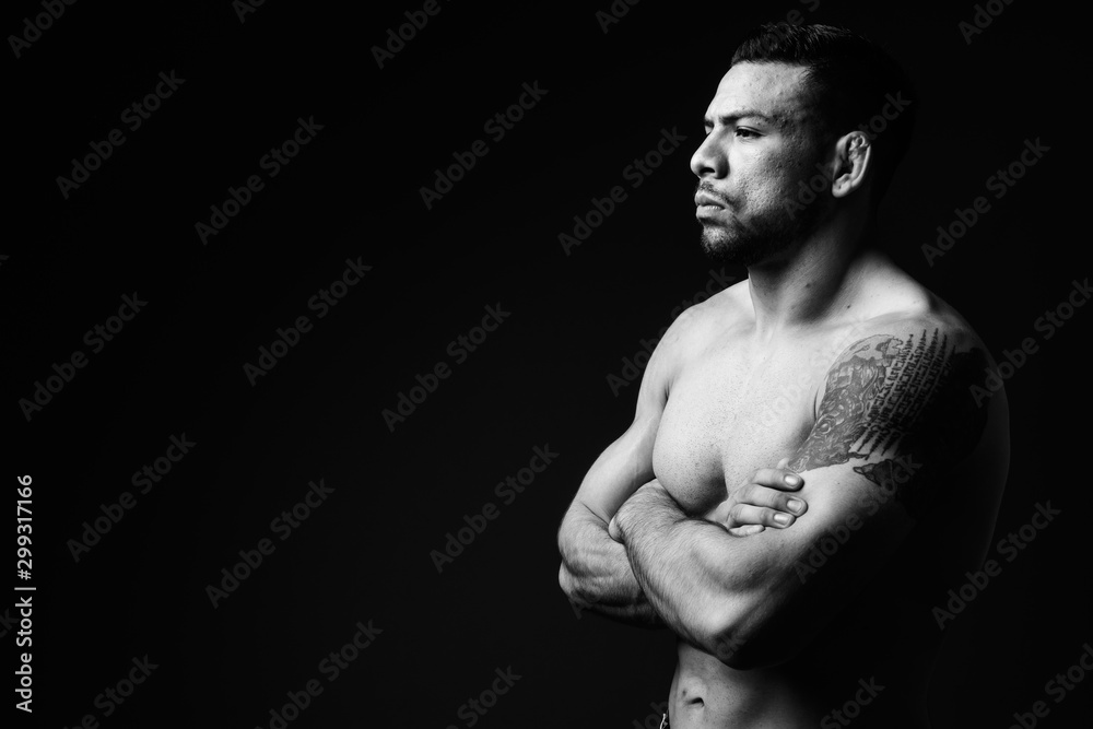 Young muscular Hispanic man shirtless against black background
