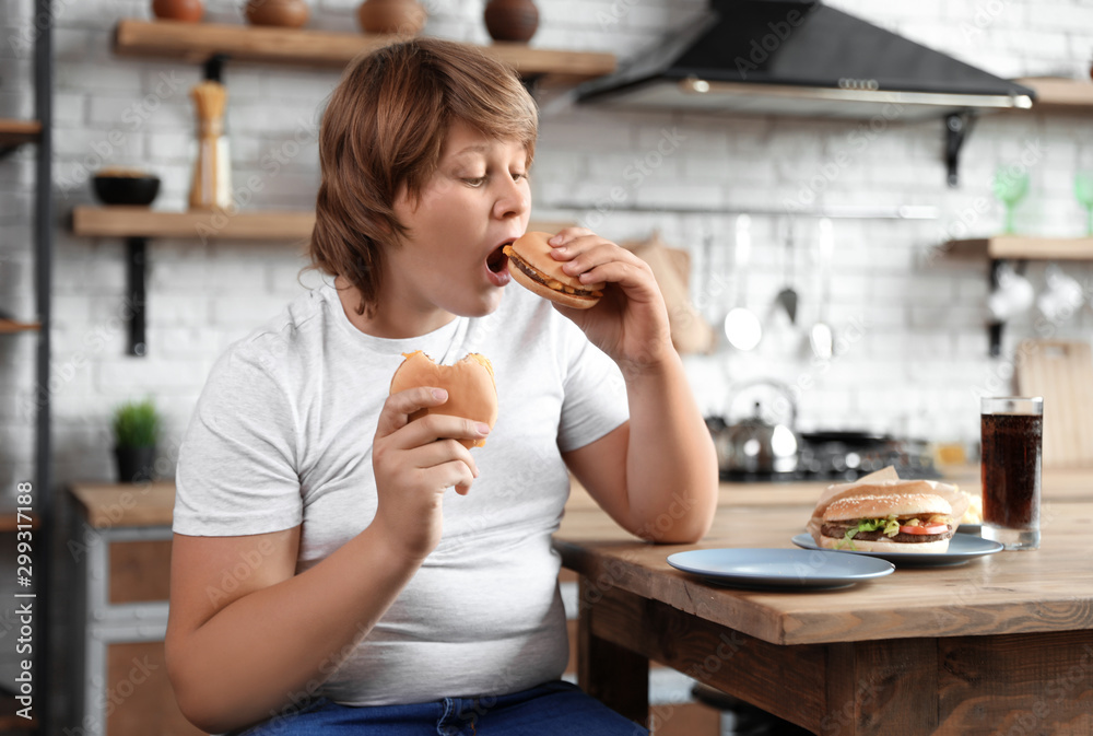 Overweight boy at table with fast food in kitchen Stock Photo | Adobe Stock