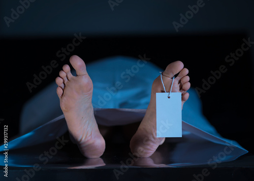 Cadaver on autopsy table at morgue, label tied to toe, close-up photo