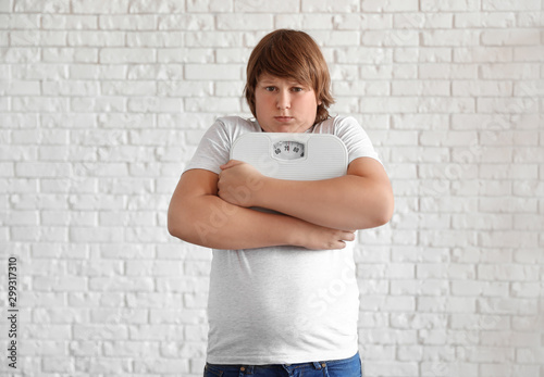 Emotional overweight boy with floor scales near white brick wall photo