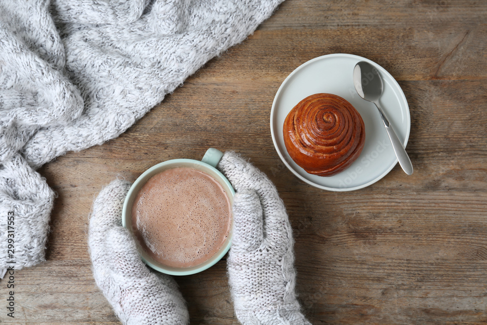 Woman with delicious cocoa drink and hot bun at wooden table, top view - obrazy, fototapety, plakaty 