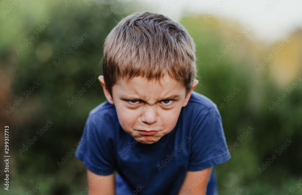 Portrait of a little boy on a blurry green nature background. The child is angry and looks in the frame Portrait of a little boy on a blurry green nature background. The child is angry and looks in the frame