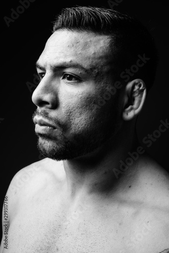 Young muscular Hispanic man shirtless against black background