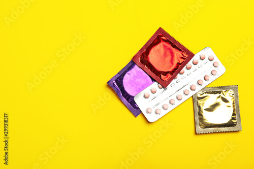 Condoms and birth control pills on yellow background, flat lay with space for text. Safe sex concept