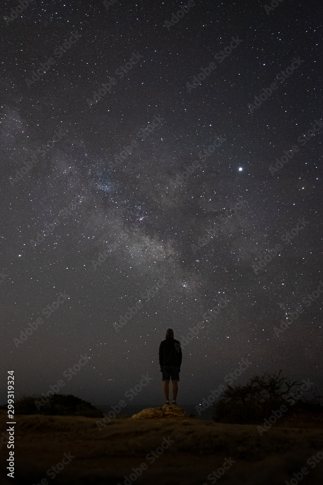 A person is standing next to the Milky Way galaxy in Algarve, Portugal. Starry night sky with man silhouette.