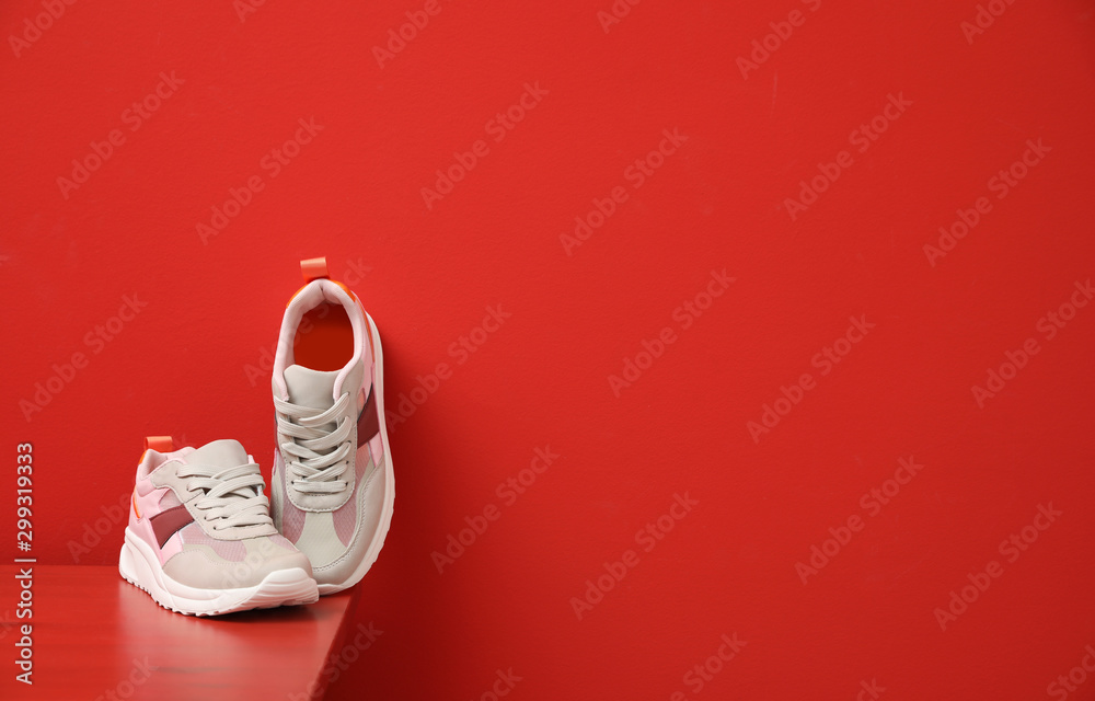 Stylish women's sneakers on wooden table near red wall, space for text - obrazy, fototapety, plakaty 
