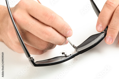 Handyman repairing sunglasses with screwdriver on white background, closeup