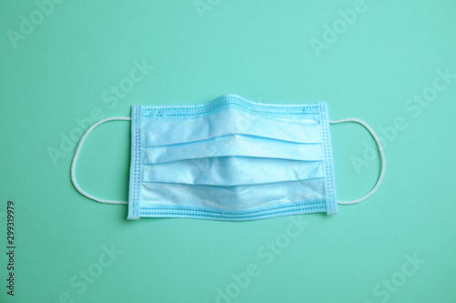 Medical face mask on turquoise background, top view