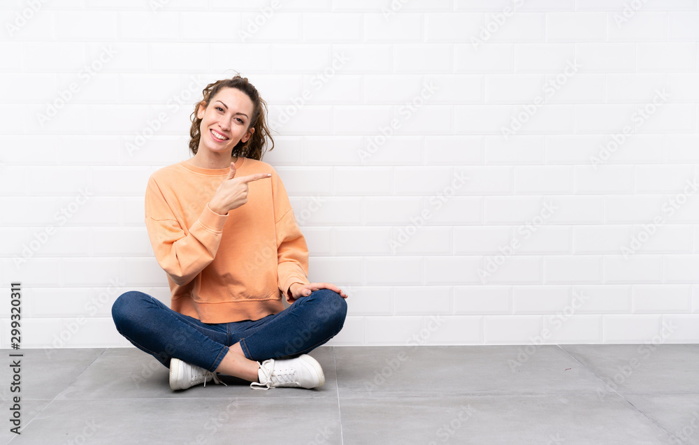 Young woman with curly hair sitting on the floor pointing finger to the side Young woman with curly hair sitting on the floor pointing finger to the side