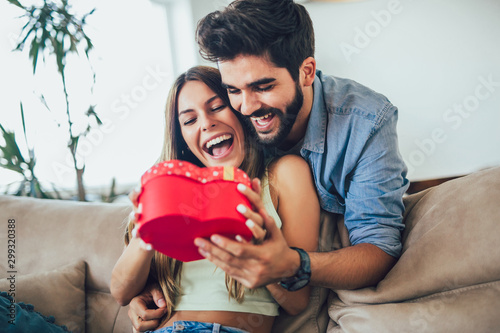 Happy couple with gift box hugging at home. Handsome man is giving his girlfriend a gift box photo