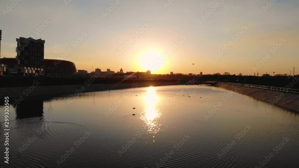 Aerial flying over ducks floating peacefully in a city park. Ducks are swimming on the water against the backdrop of a cityscape with tall buildings. Taken by drone in the sunset Aerial flying over ducks floating peacefully in a city park. Ducks are swimming on the water against the backdrop of a cityscape with tall buildings. Taken by drone in the sunset