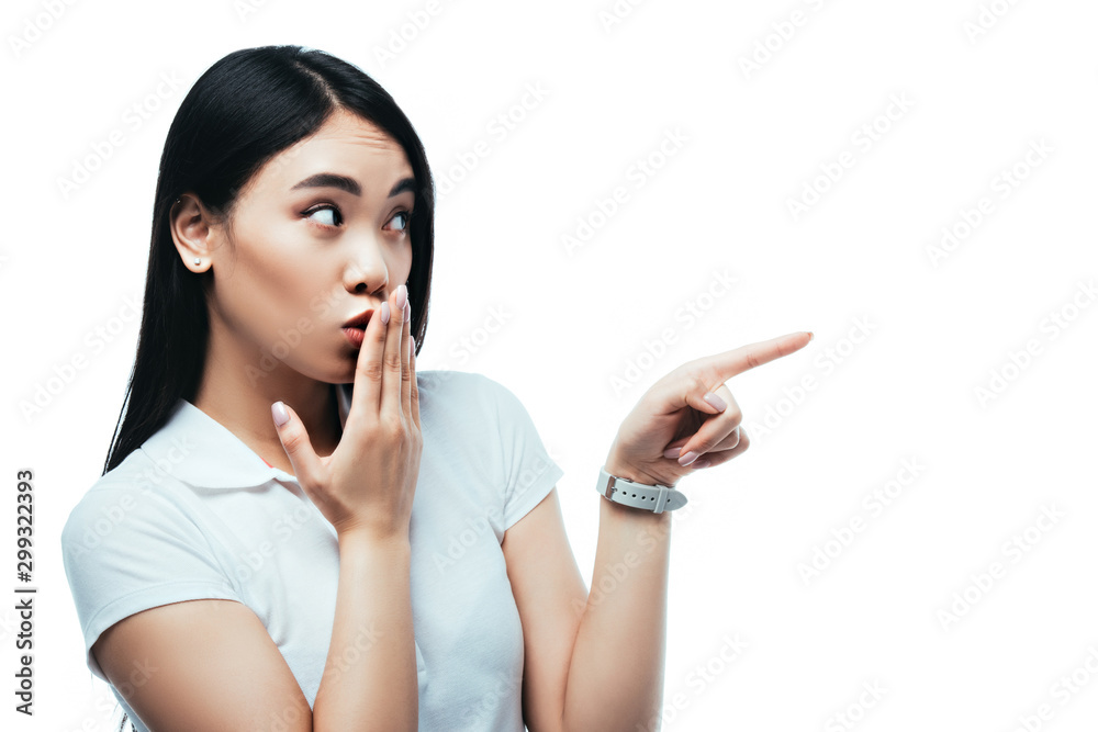 surprised attractive asian girl covering mouth with hand and pointing with finger isolated on white surprised attractive asian girl covering mouth with hand and pointing with finger isolated on white