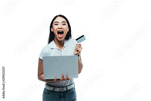 excited attractive asian girl with open mouth holding credit card and laptop isolated on white
