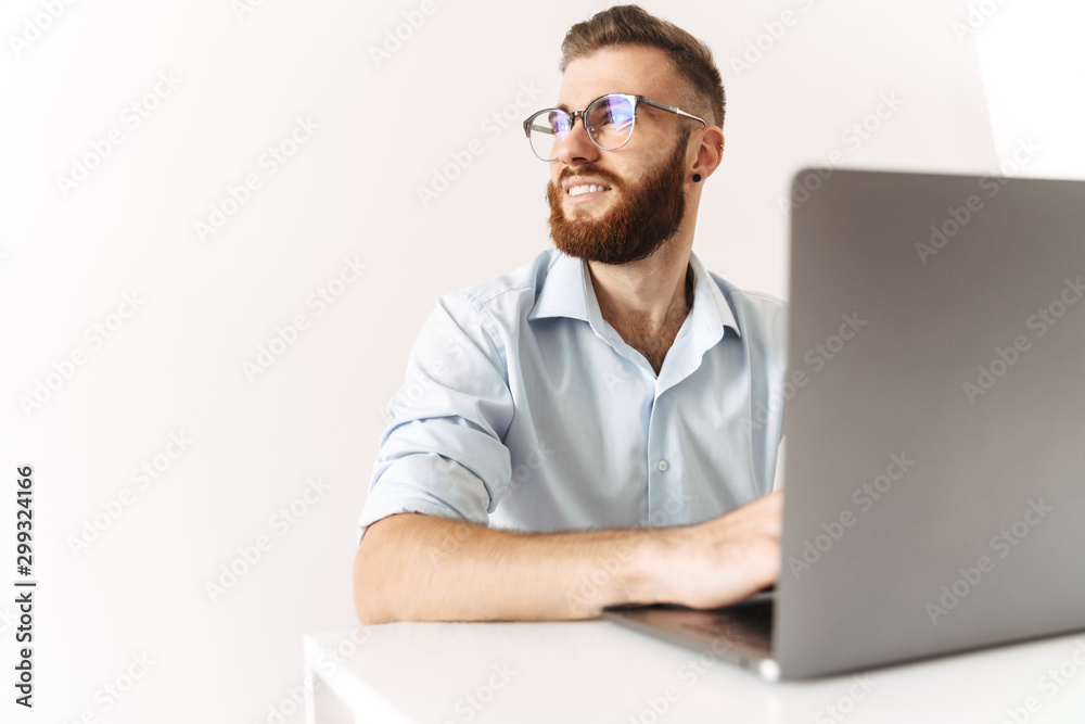 Image of young man wearing eyeglasses working on laptop in office Image of young man wearing eyeglasses working on laptop in office
