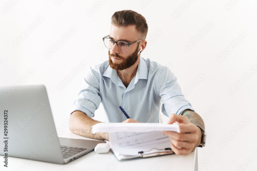 Image of man in eyeglasses working on laptop with documents in office Image of man in eyeglasses working on laptop with documents in office