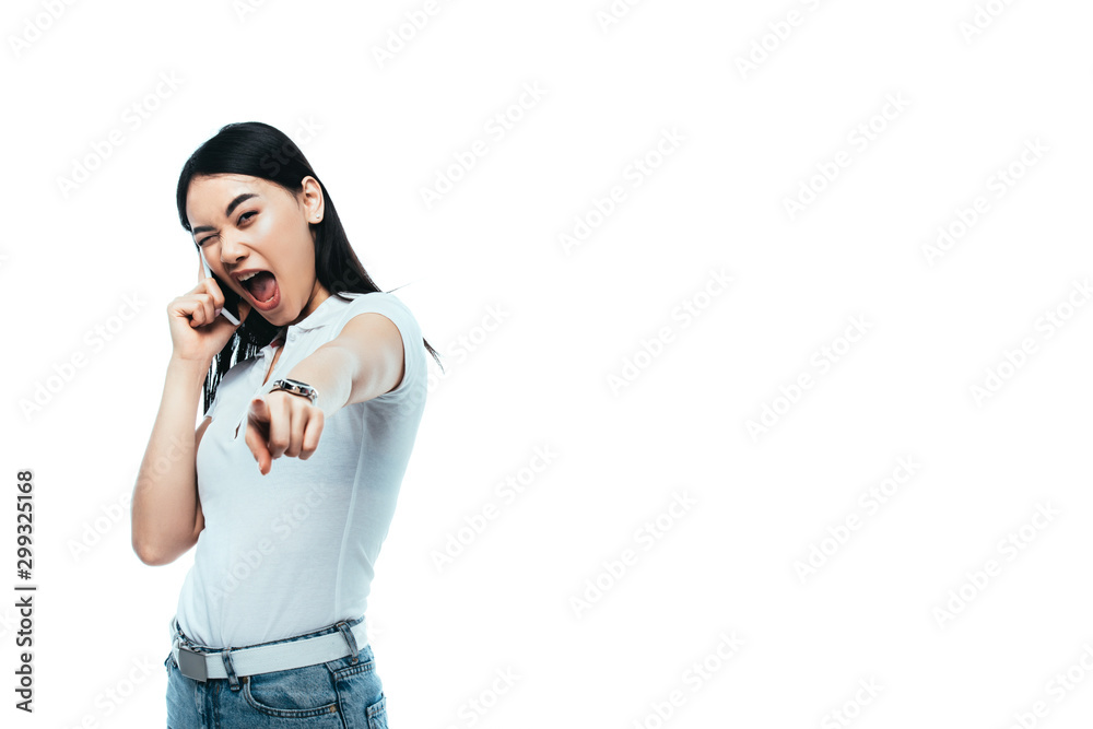 excited brunette asian woman talking on smartphone and pointing with finger at camera isolated on white excited brunette asian woman talking on smartphone and pointing with finger at camera isolated on white