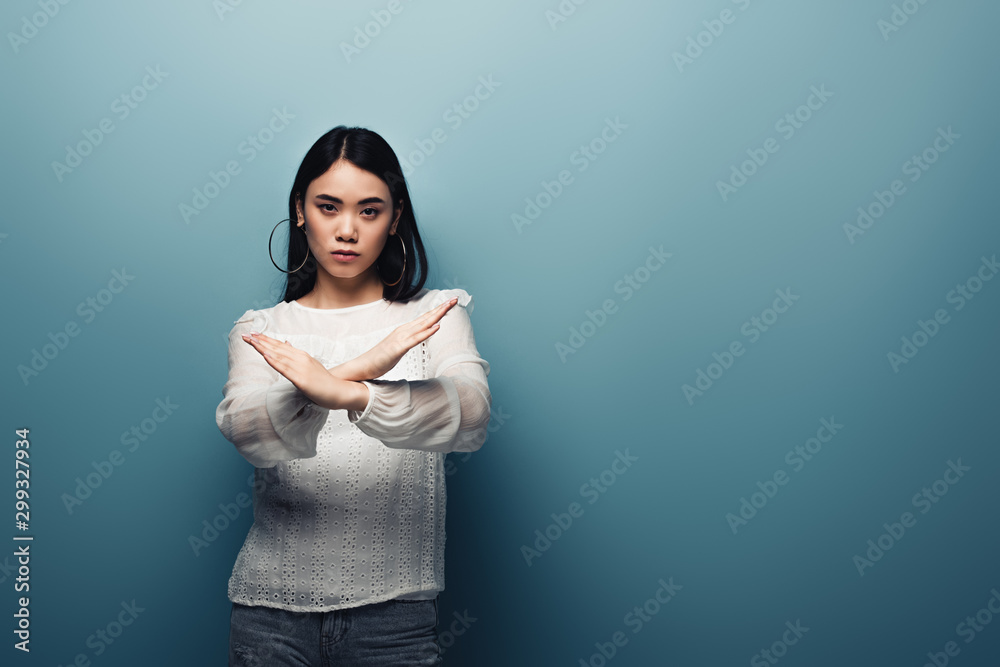 upset brunette asian woman showing stop gesture on blue background upset brunette asian woman showing stop gesture on blue background