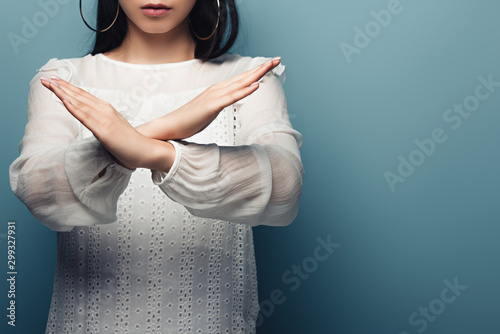 cropped view of brunette asian woman showinng stop gesture on blue background photo