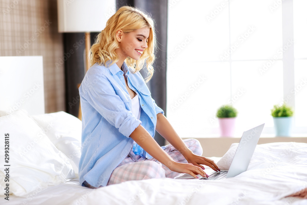 happy young cheerful  girl with computer at home in bed working and laughing. - obrazy, fototapety, plakaty 