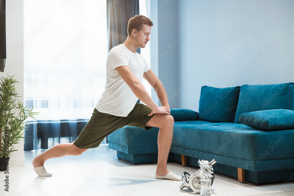Fototapeta premium young handsome man doing lunges during stretching before workout at home looking focused sporty and healthy lifestyle