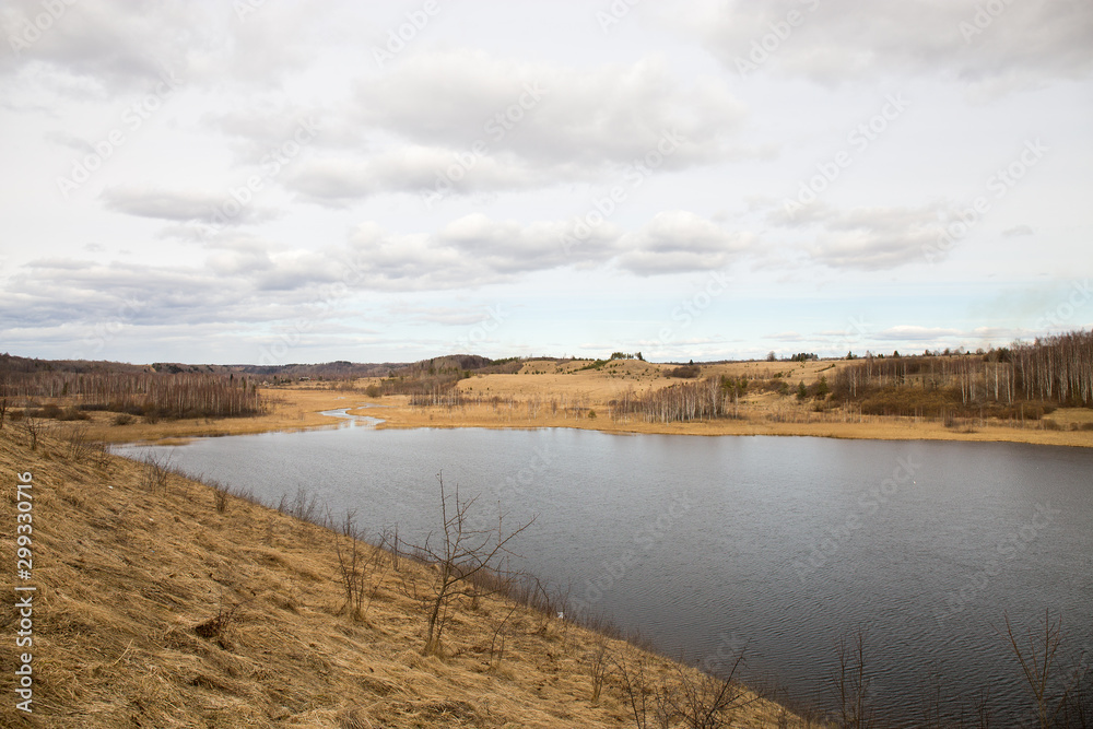 Panorama of the spring landscape with a lake and hills with copses. Izborsk, Pskov region, Russia.