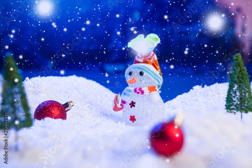 Snowman with Christmas balls on snow over fir-tree, night sky and moon. Shallow depth of field. Christmas background. Fairy tale. Macro. Artificial magic dreamy world. © Alik Mulikov