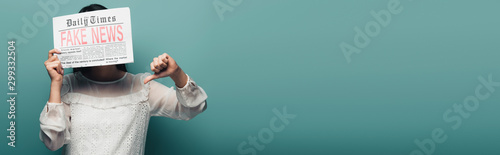 woman in white blouse holding newspaper with fake news and showing thumb down on green background
