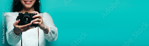 cropped view of smiling asian woman in white blouse holding digital camera on turquoise background, panoramic shot