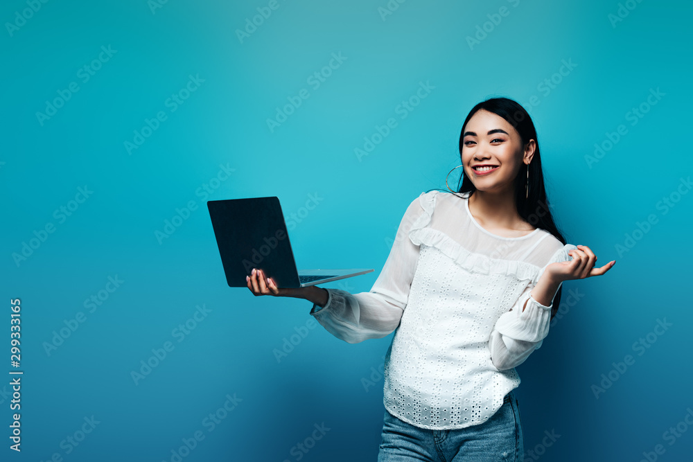 smiling asian woman in white blouse holding laptop on blue background smiling asian woman in white blouse holding laptop on blue background