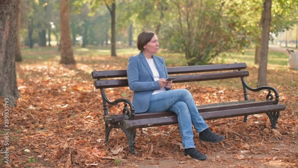 Businesswoman using mobile phone on park bench in autumn Businesswoman using mobile phone on park bench in autumn