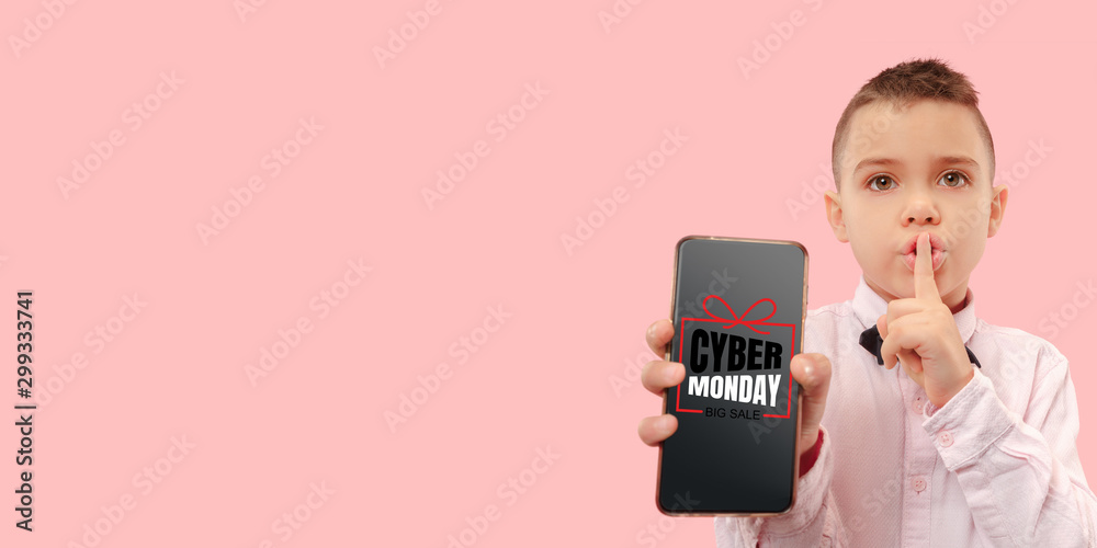 Portrait of young caucasian boy showing smartphone screen on coral background. Whispering a secret. Concept of sales, black friday, cyber monday, finance, business. Online shops and payments bill. Portrait of young caucasian boy showing smartphone screen on coral background. Whispering a secret. Concept of sales, black friday, cyber monday, finance, business. Online shops and payments bill.