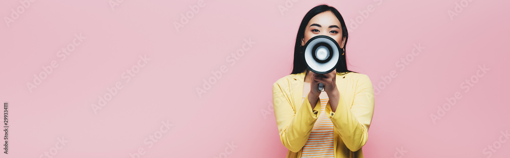 Fototapeta premium asian woman in yellow outfit holding megaphone isolated on pink, panoramic shot