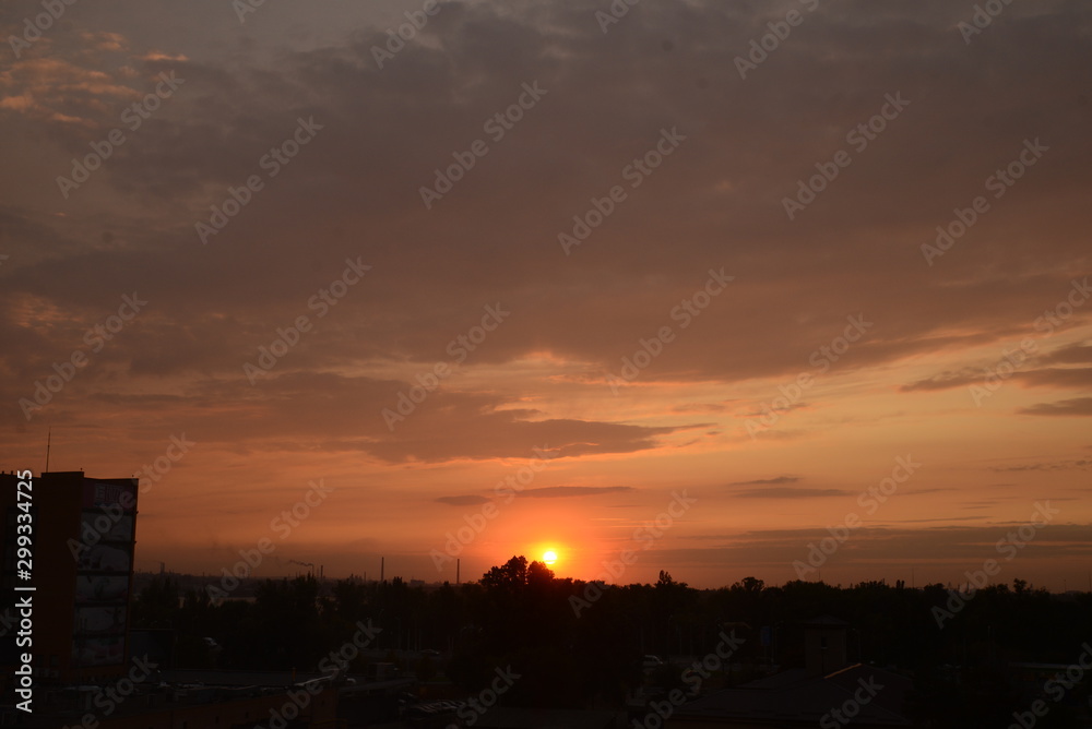 View of the dramatic sky above the sity at sunset with dark blue clouds and pink, purple and yellow flashes from the sun's rays View of the dramatic sky above the sity at sunset with dark blue clouds and pink, purple and yellow flashes from the sun's rays