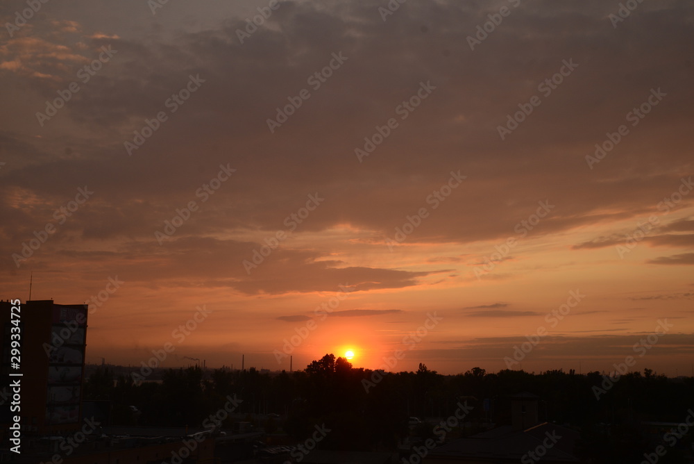 View of the dramatic sky above the sity at sunset with dark blue clouds and pink, purple and yellow flashes from the sun's rays