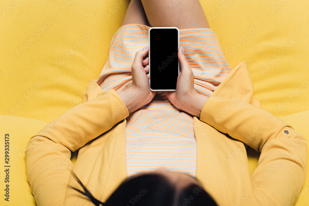 overhead view of businesswoman sitting on yellow sofa and holding smartphone with blank screen overhead view of businesswoman sitting on yellow sofa and holding smartphone with blank screen