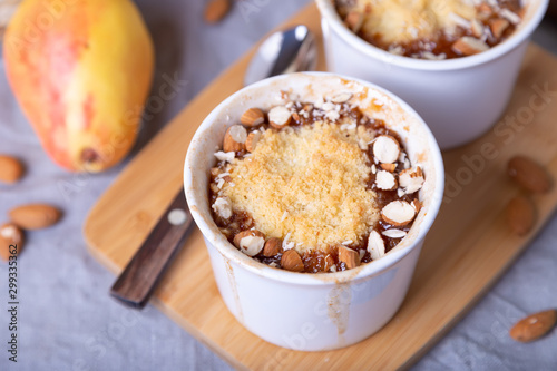 Crumble with caramelized pear, cinnamon and almonds in a white ramekin. Close-up.